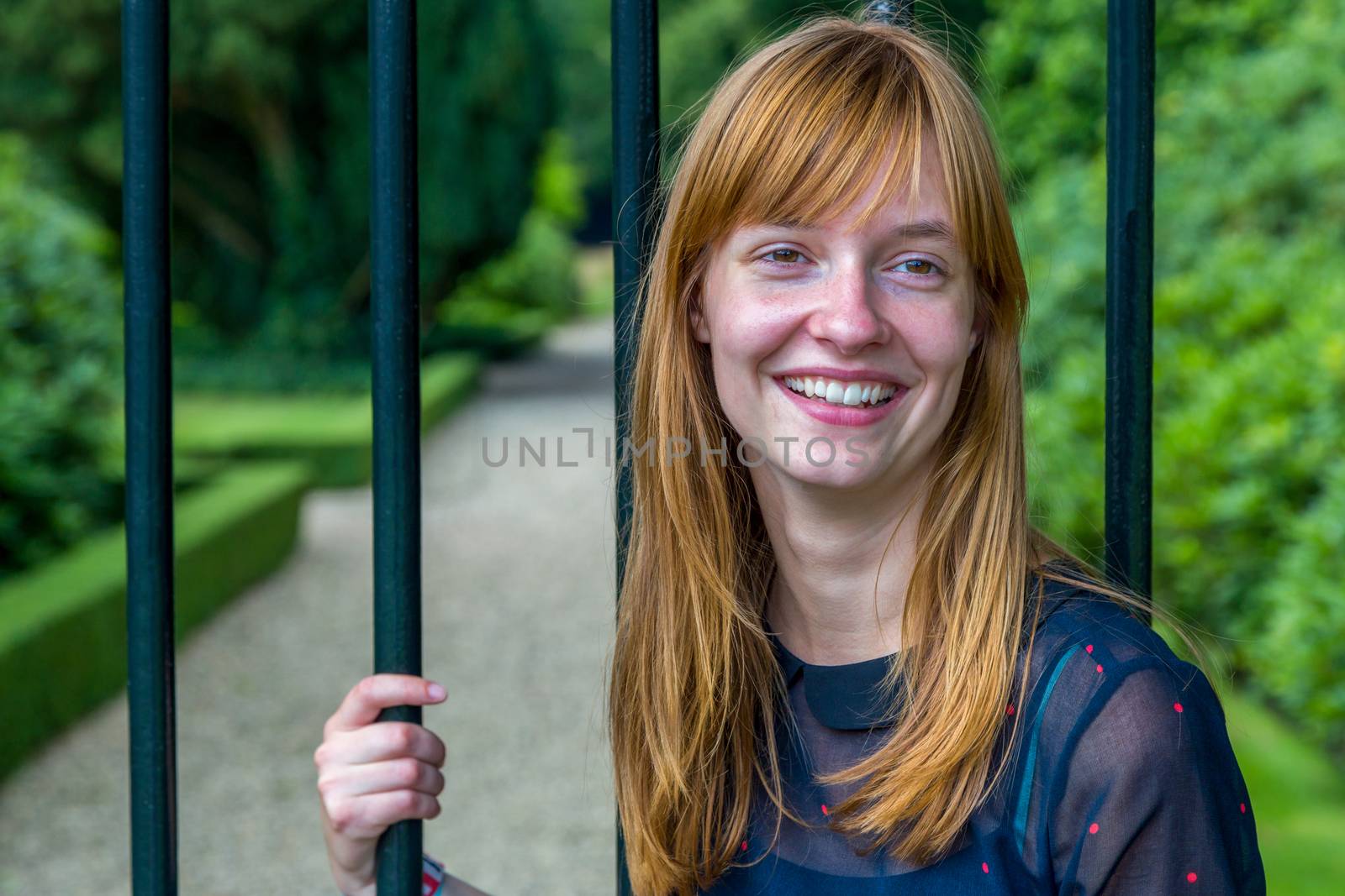 Red haired dutch teenage girl laughing holding metal bar of gate