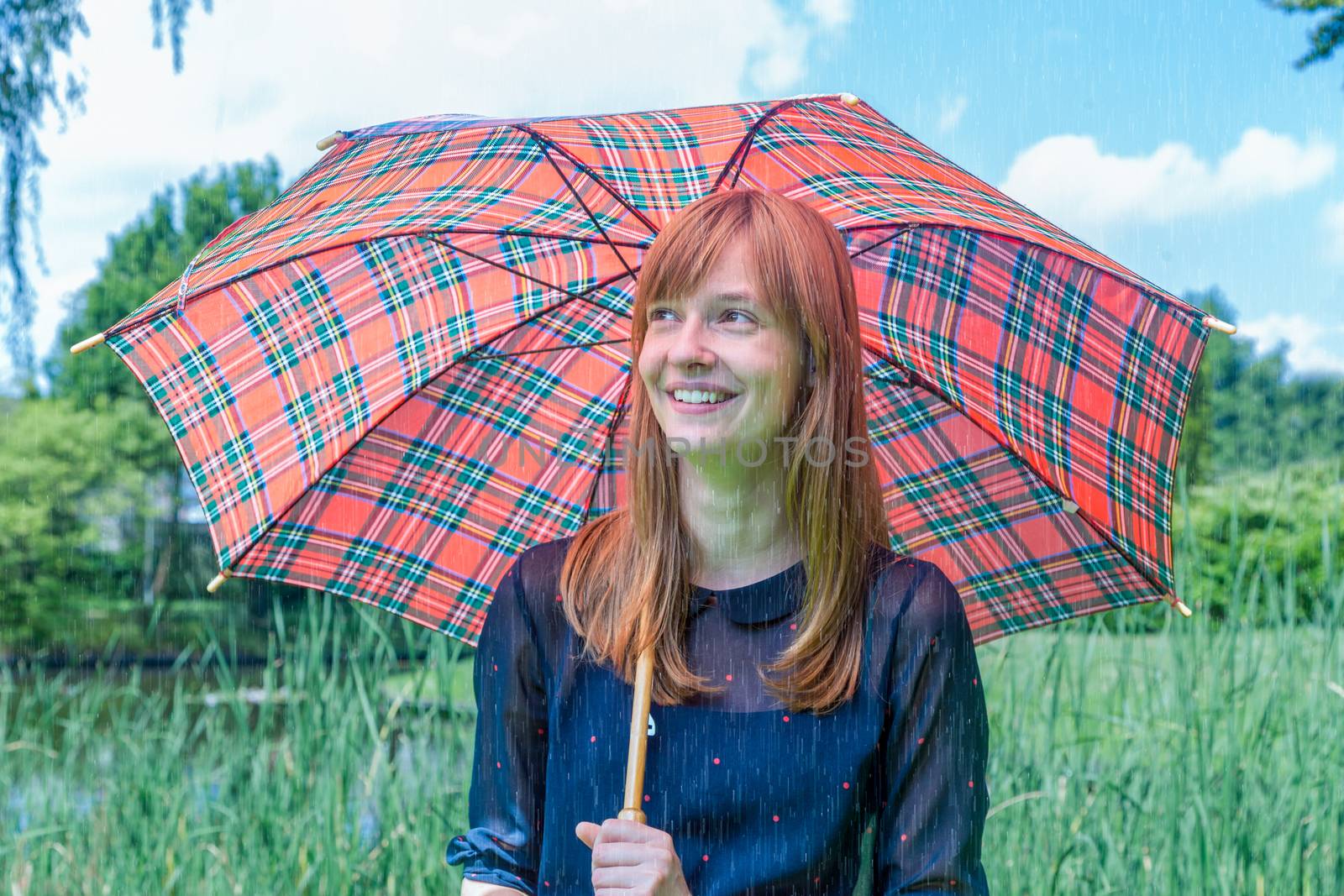 Caucasian teenage girl holding  umbrella on rainy day in green nature