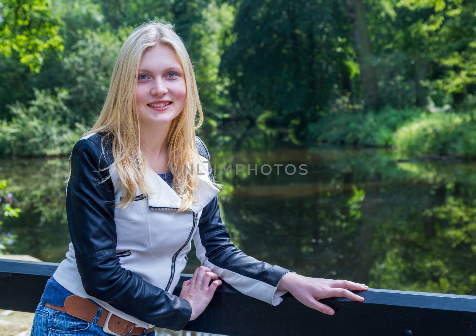 Blond girl leaning on fence near water in forest by BenSchonewille