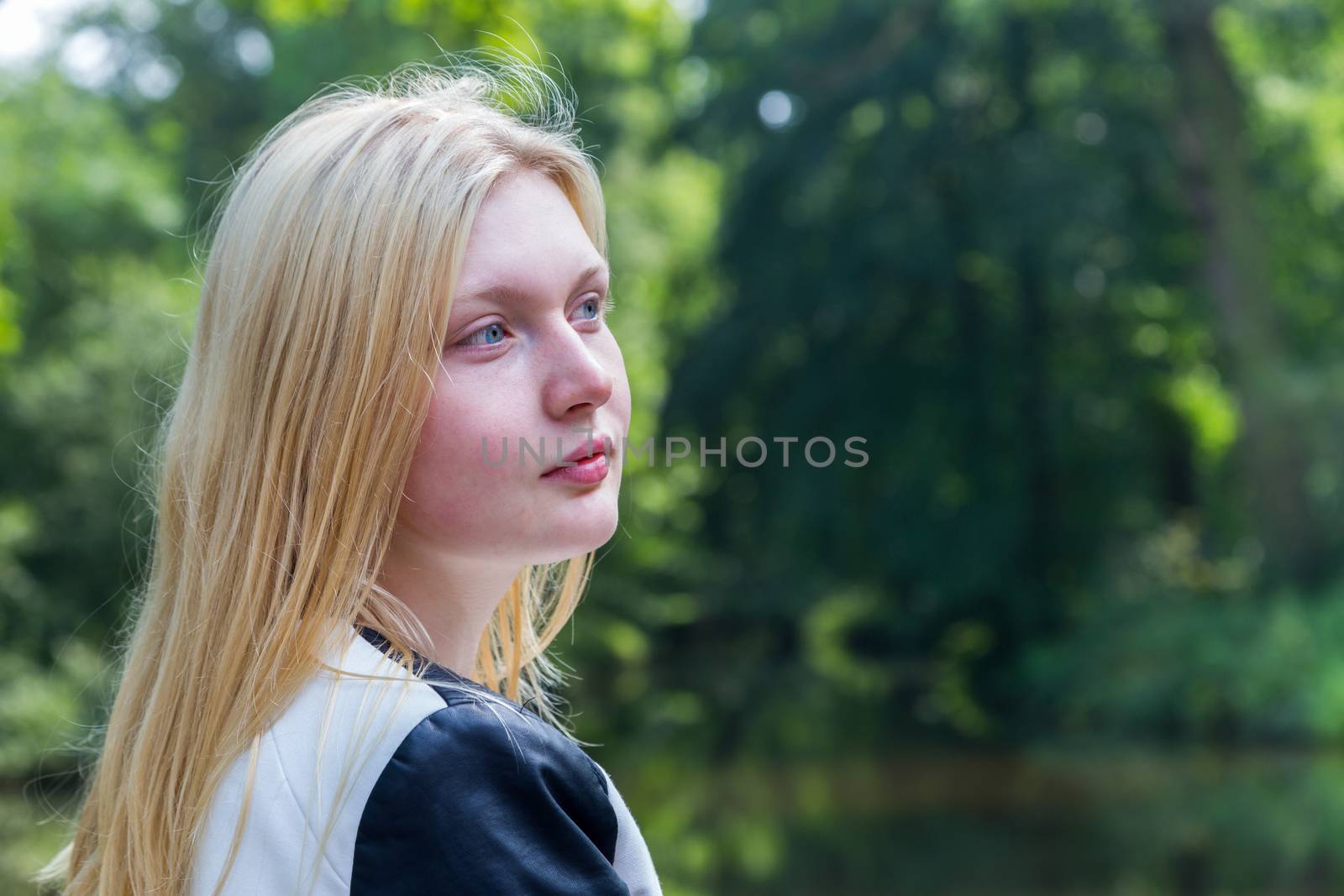 Head of blond dutch teenage girl with water and trees in park