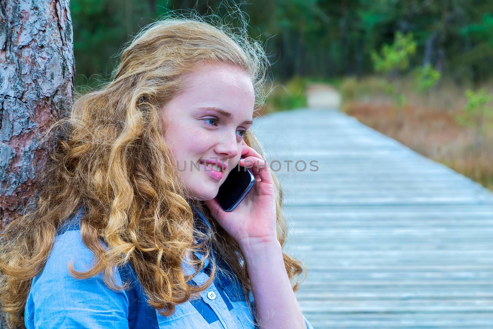 Blonde caucasian teenage girl phoning with mobile telephone in nature