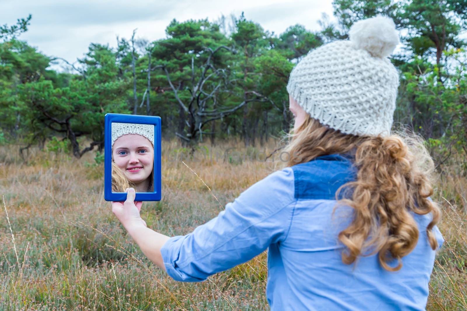 Blonde dutch teenage girl with long hair looking in mirror with forest background