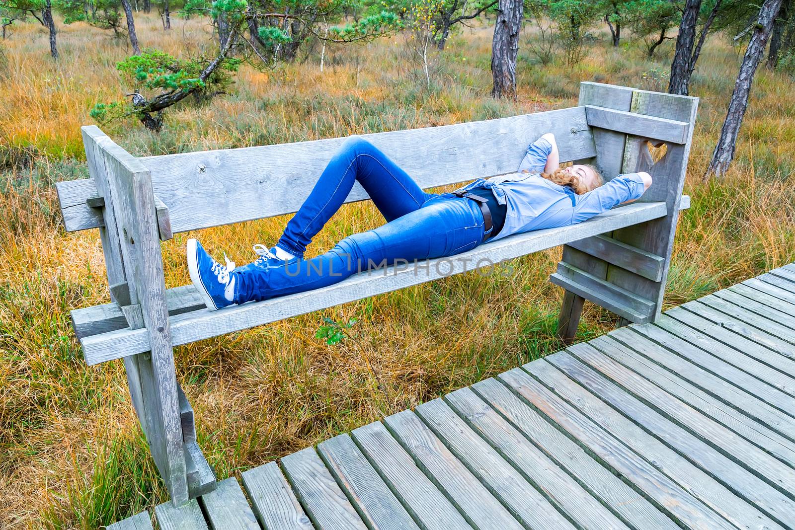 Teenage girl lying on wooden bench near path in forest