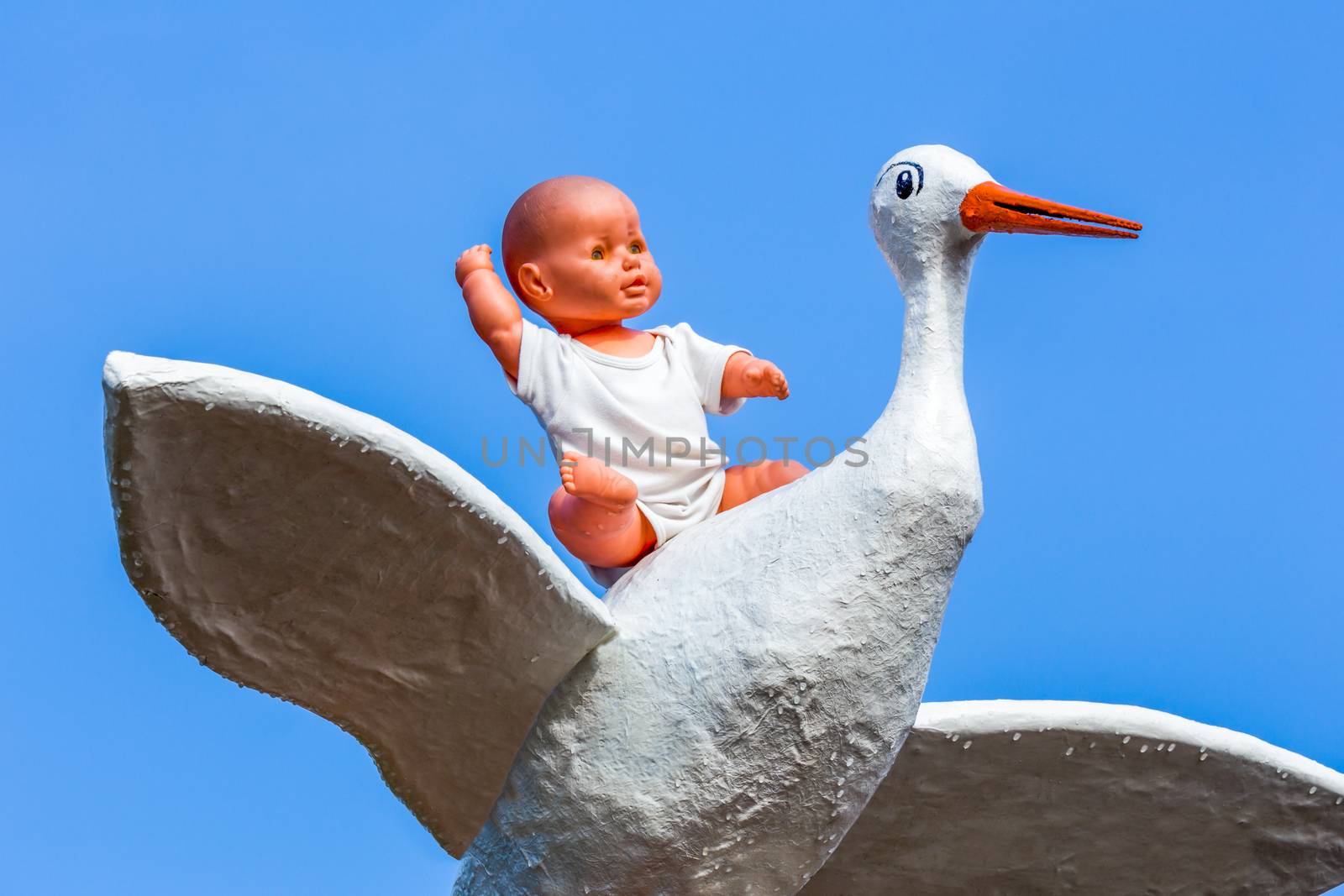 Baby doll sitting on stork with blue sky