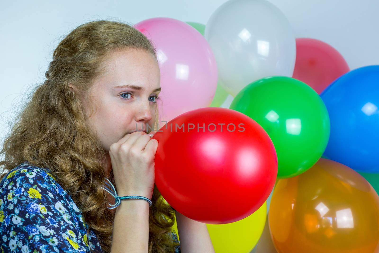 Teenage girl blowing inflating colored balloons by BenSchonewille