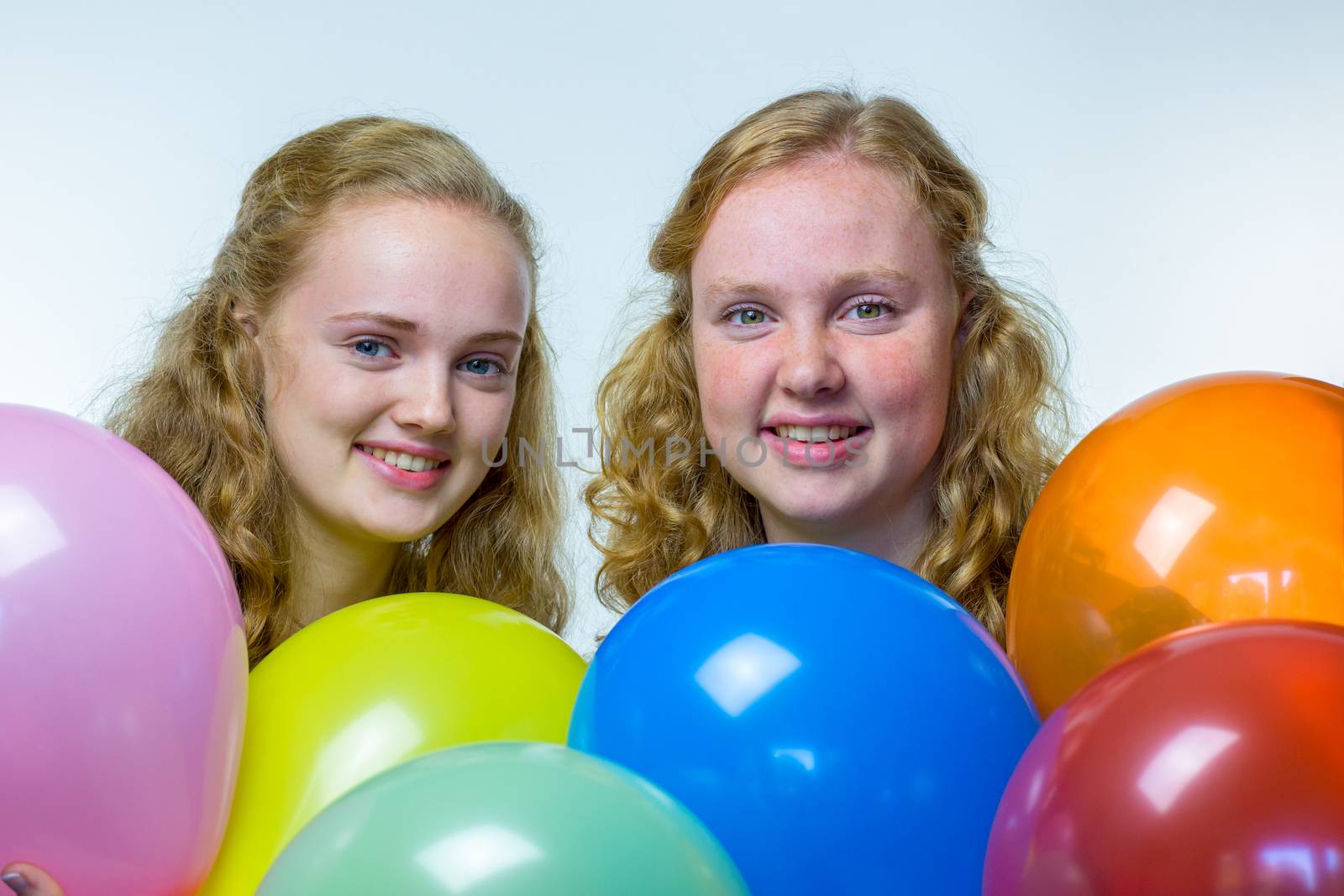 Two european teenage girls heads behind colored balloons isolated on white background