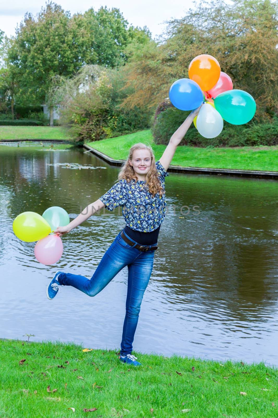 Girl standing at pond with colored balloons by BenSchonewille