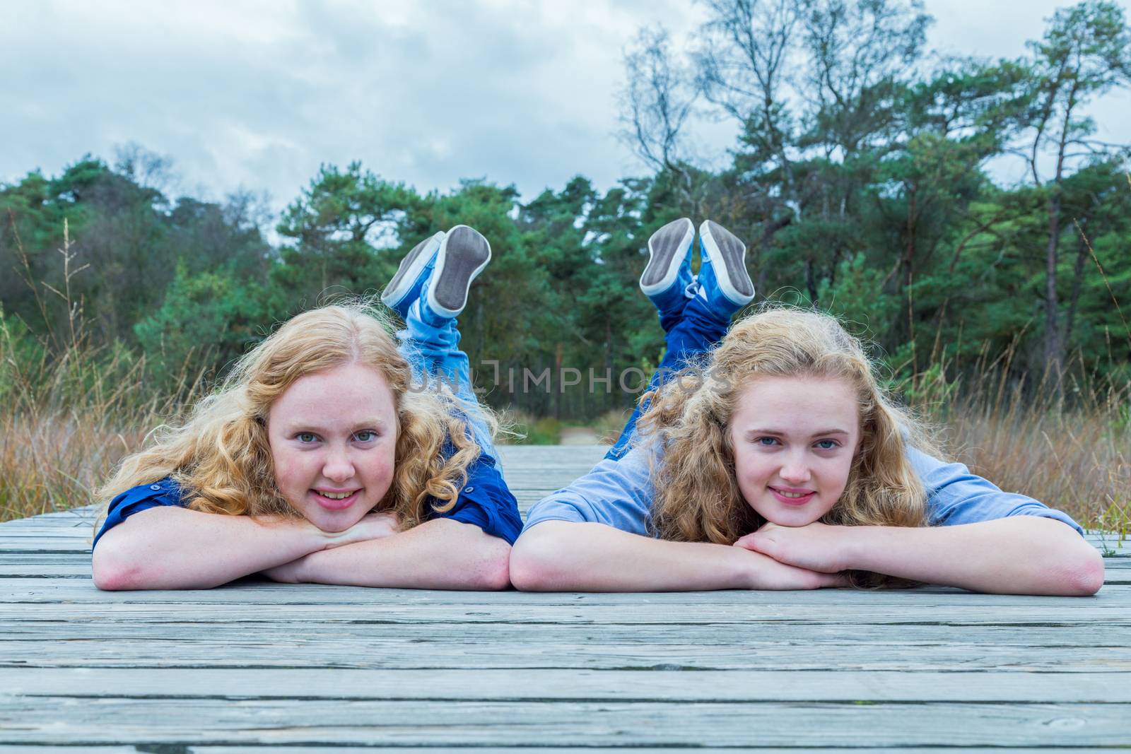 Two girls lying on wooden path in nature by BenSchonewille