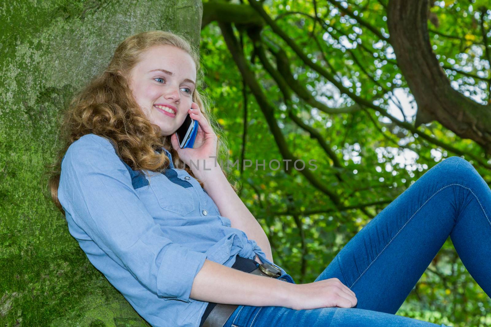Caucasian teenage girl phoning with mobile telephone in green tree