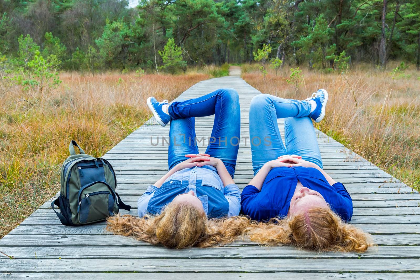 Two teenage girls lying on their backs on wooden footpath in nature