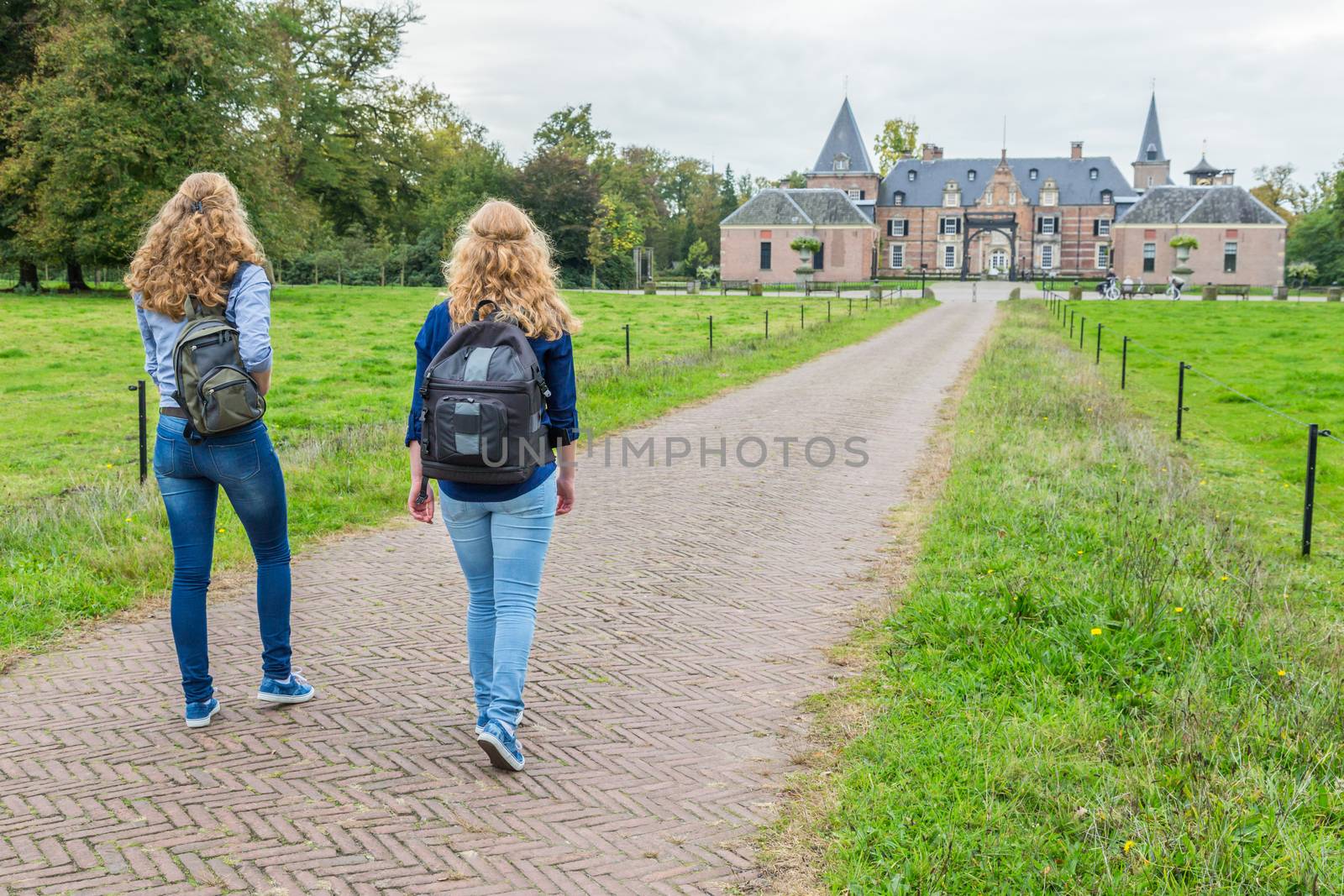 Two teenage girls walking with backpacks on road leading to castle