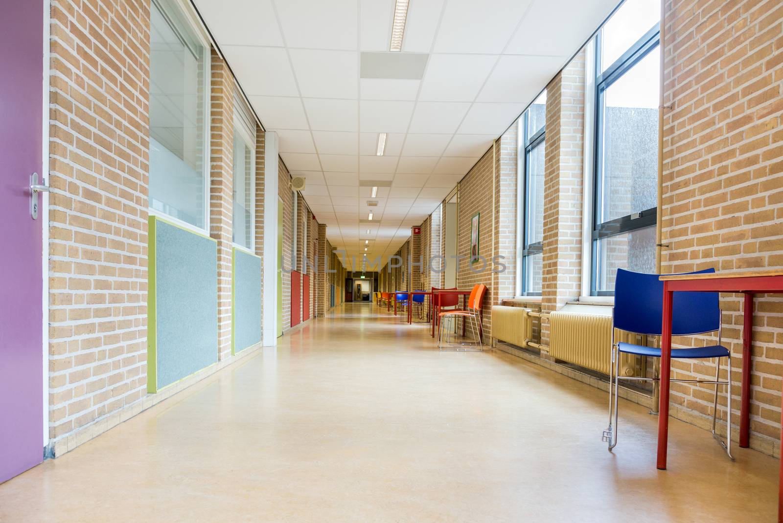 Long corridor with furniture in school building by BenSchonewille