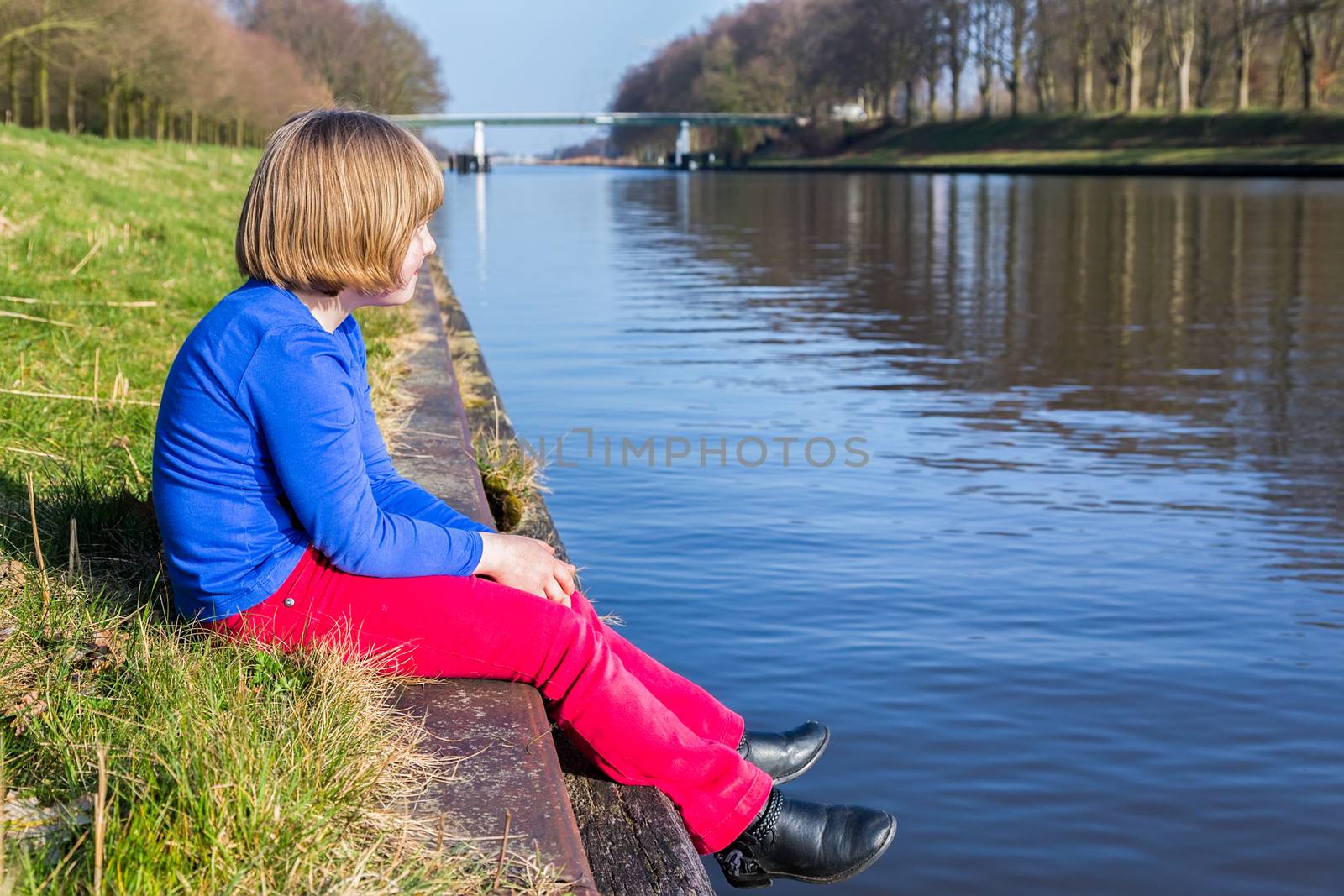 Young girl sitting at waterfront of canal by BenSchonewille