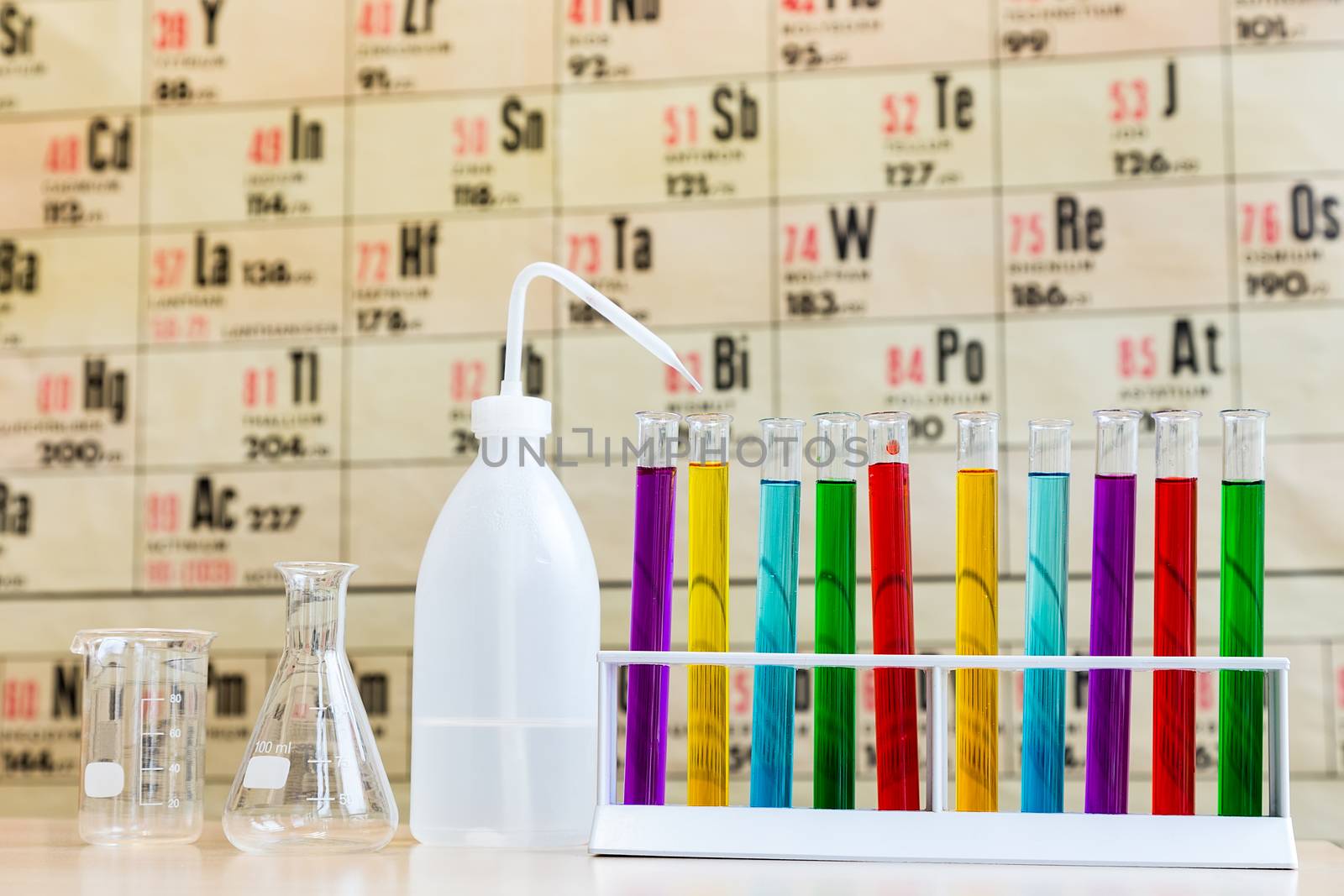 Chemistry with colored test tubes and glass in front of wallchart showing periodic table
