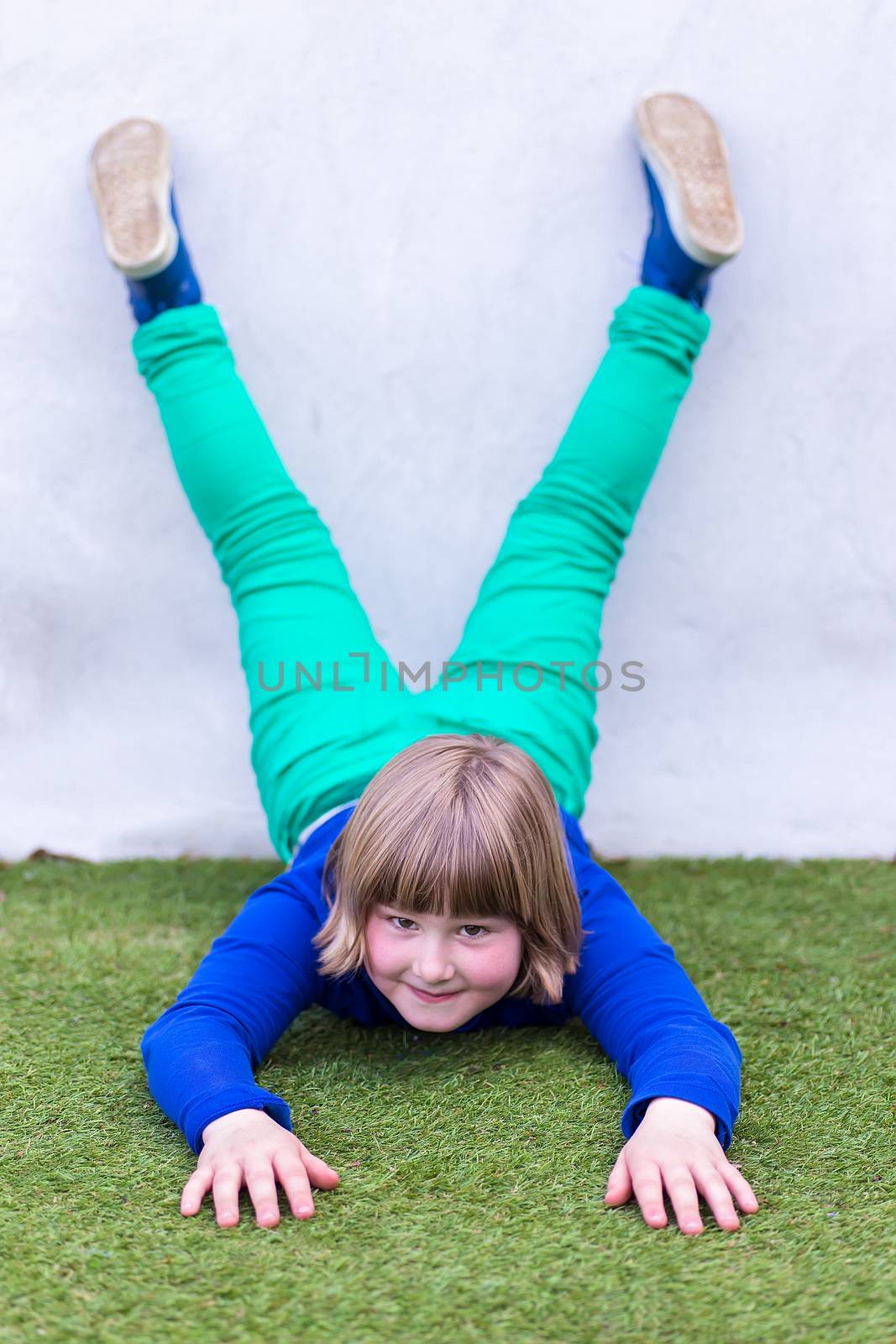 Young caucasian girl lying upside down against wall on grass at playground