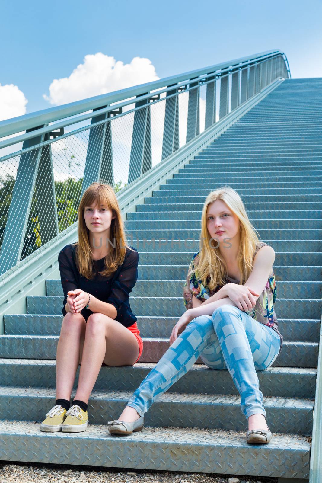 Two caucasian girls sitting on metal bridge