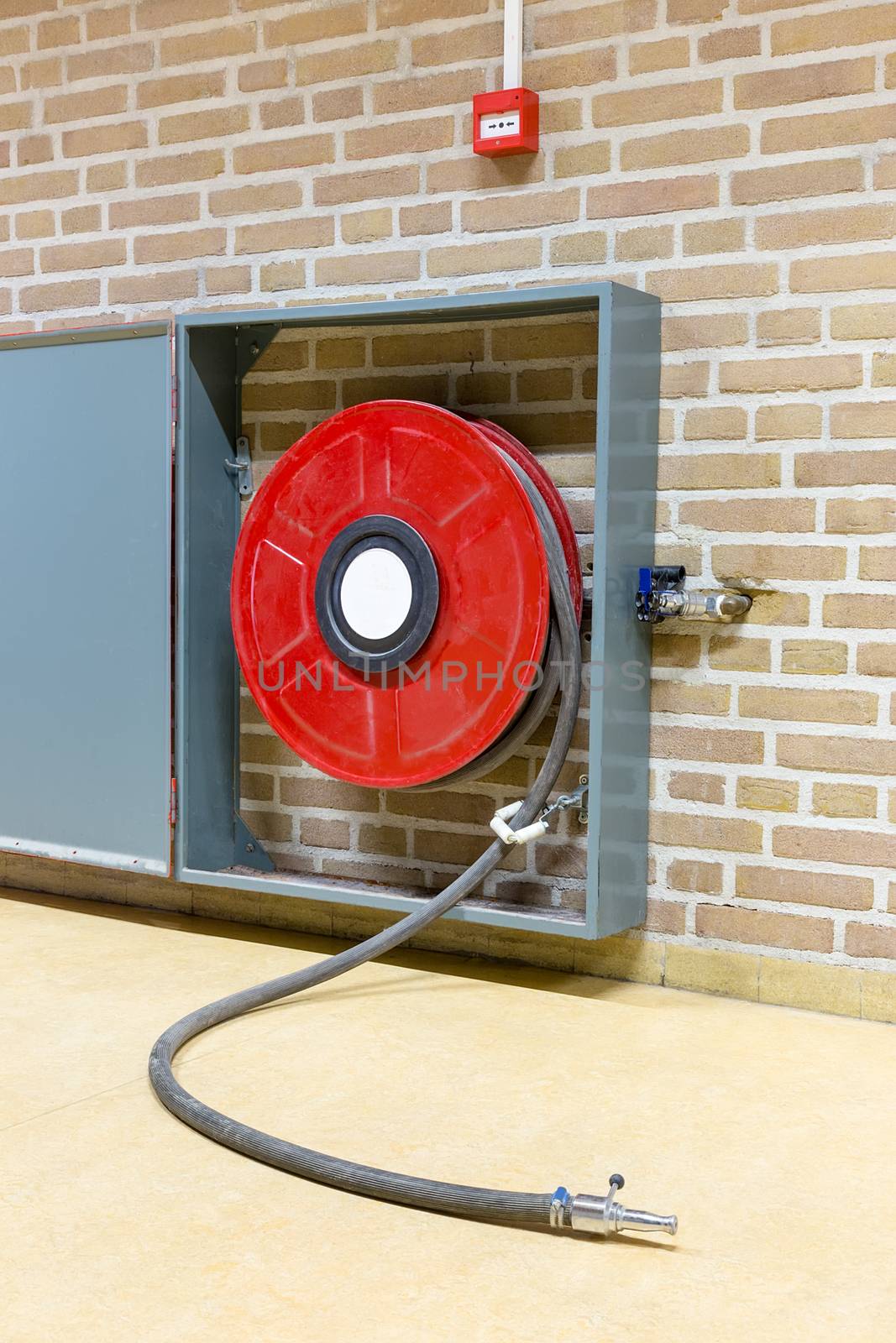 Red fire hose on reel hanging at wall in school building
