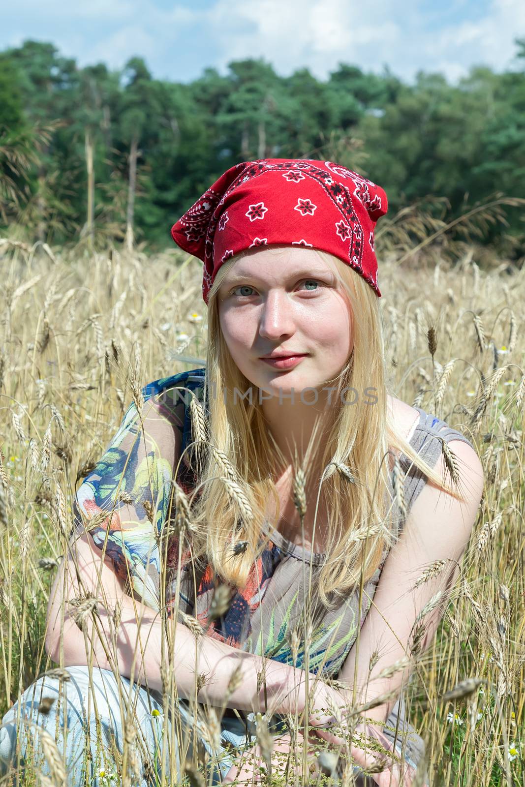 Blonde caucasian teenage girl sitting in cornfield wearing red handkerchief