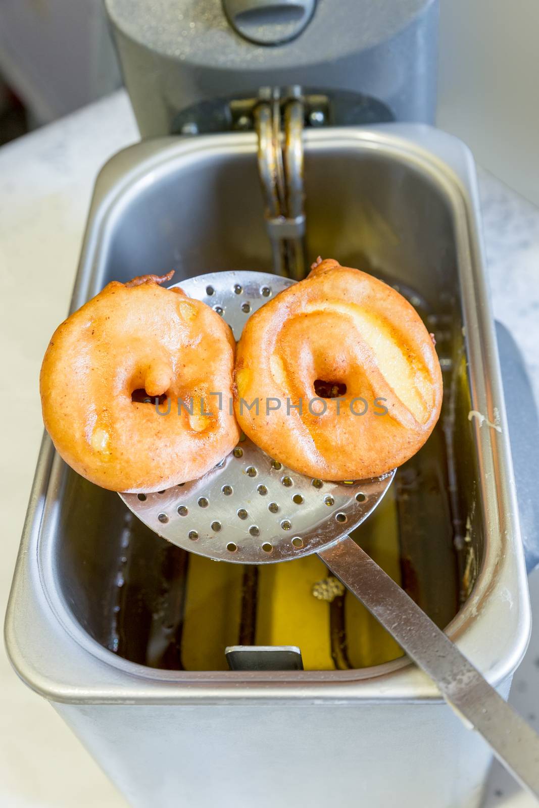 Apple turnovers on spoon above frying oil by BenSchonewille