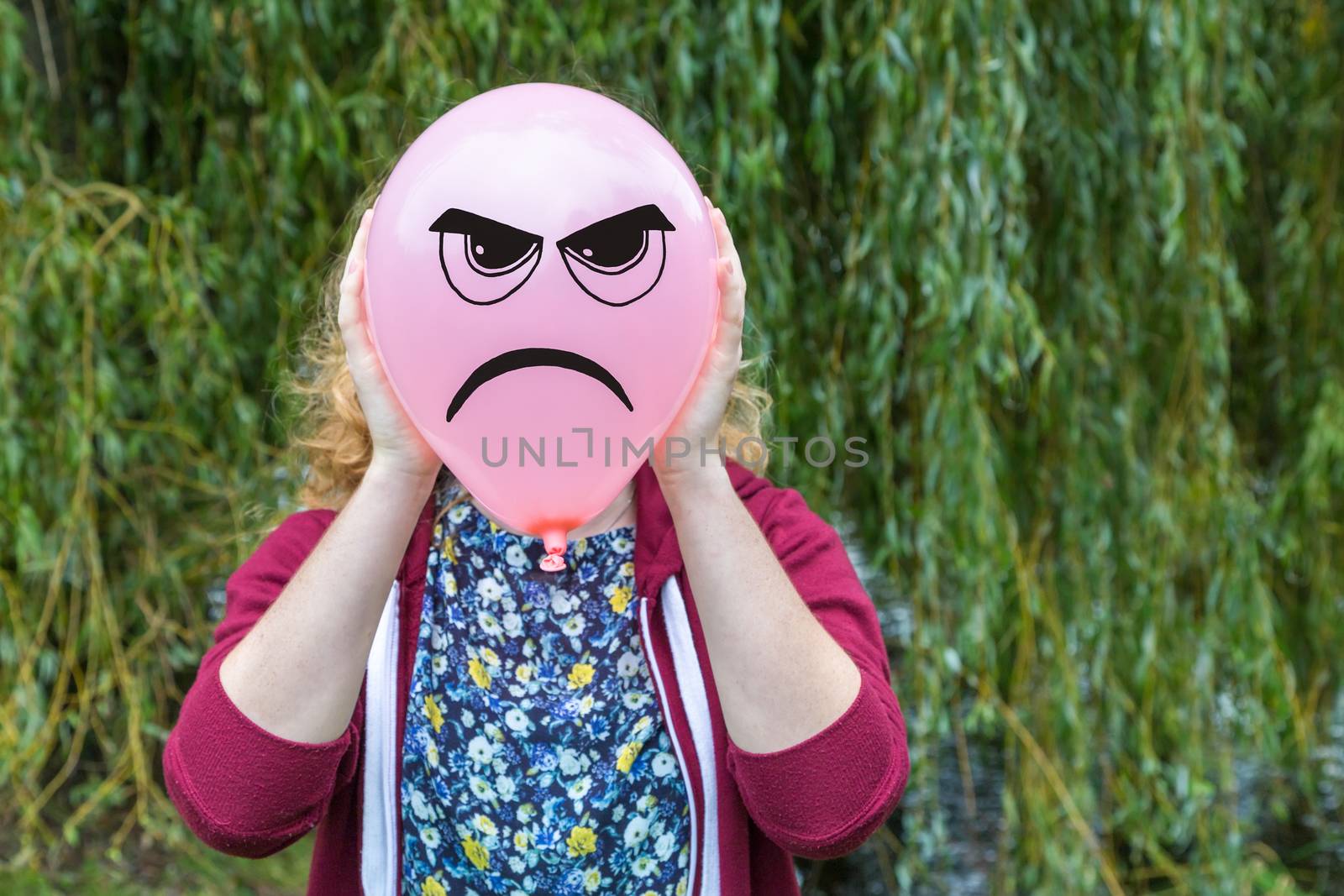 Teenage girl holding balloon with angry face as expression in nature