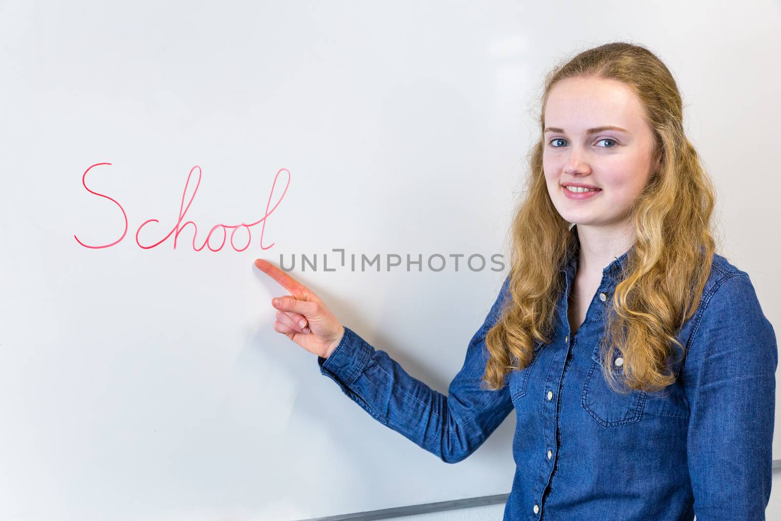 Dutch teenage girl pointing at word School written on white boar by BenSchonewille