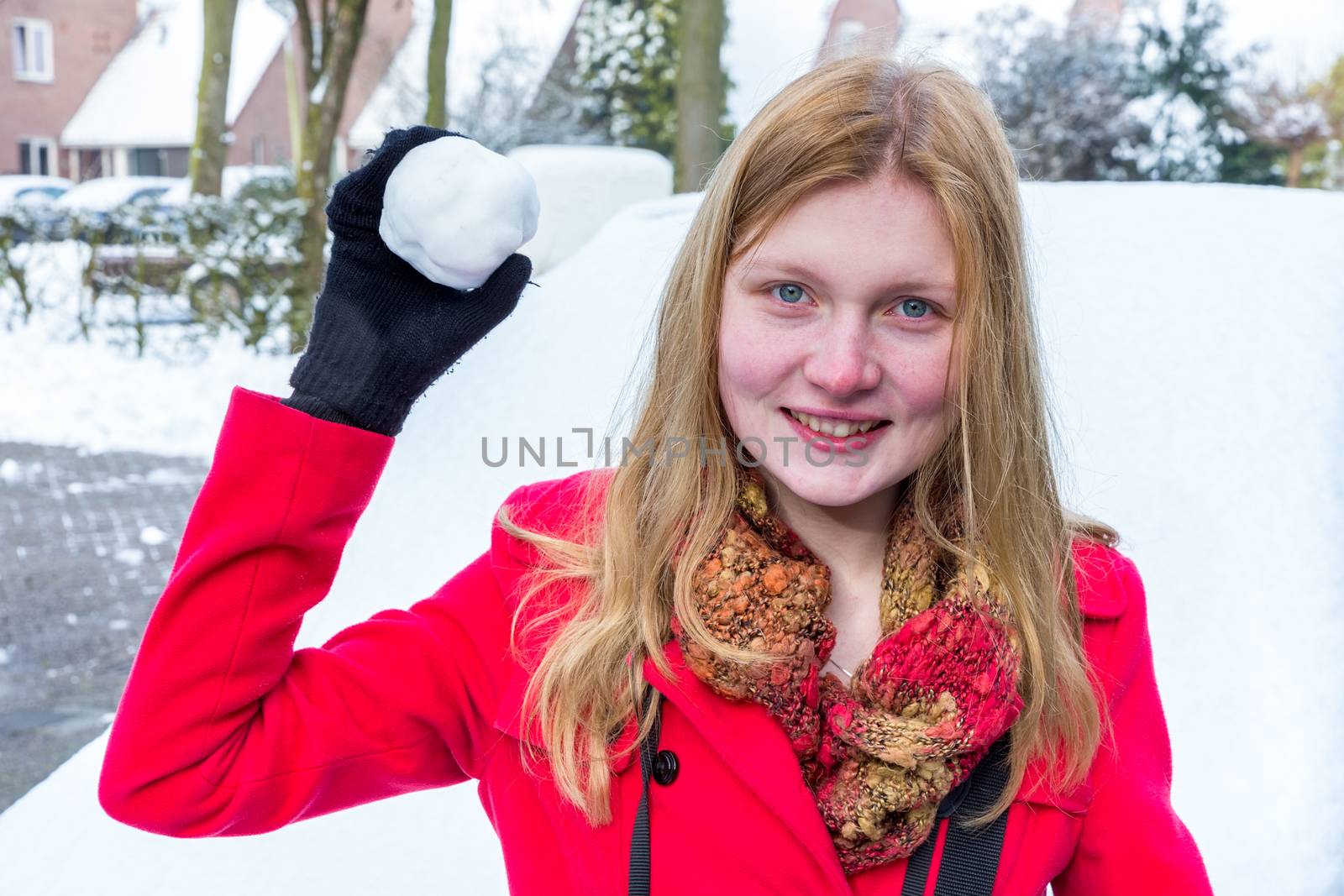 Young caucasian woman dressed in red holding snowball to throw in winter