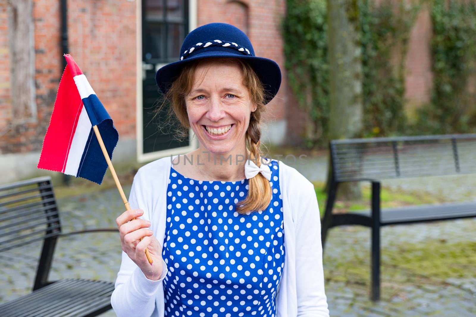 Caucasian middle aged woman dressed in blue clothes celebrating liberation day with dutch flag