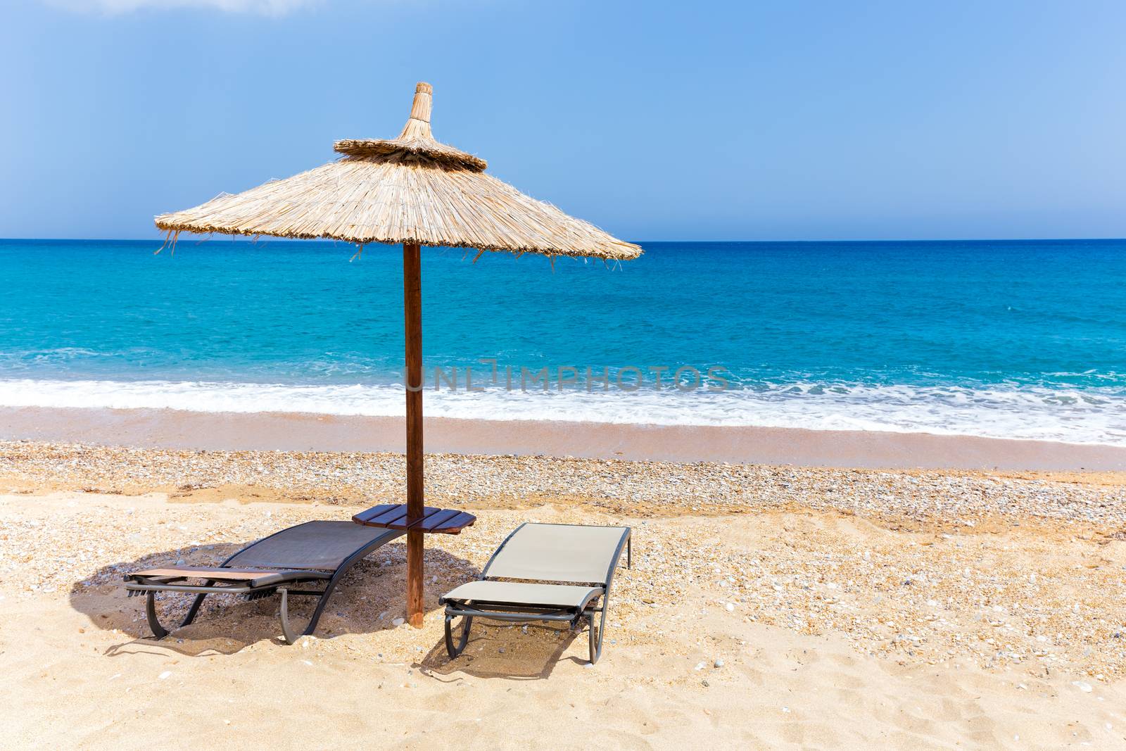 Reed beach umbrella with two loungers on beach near blue sea coast in Greece