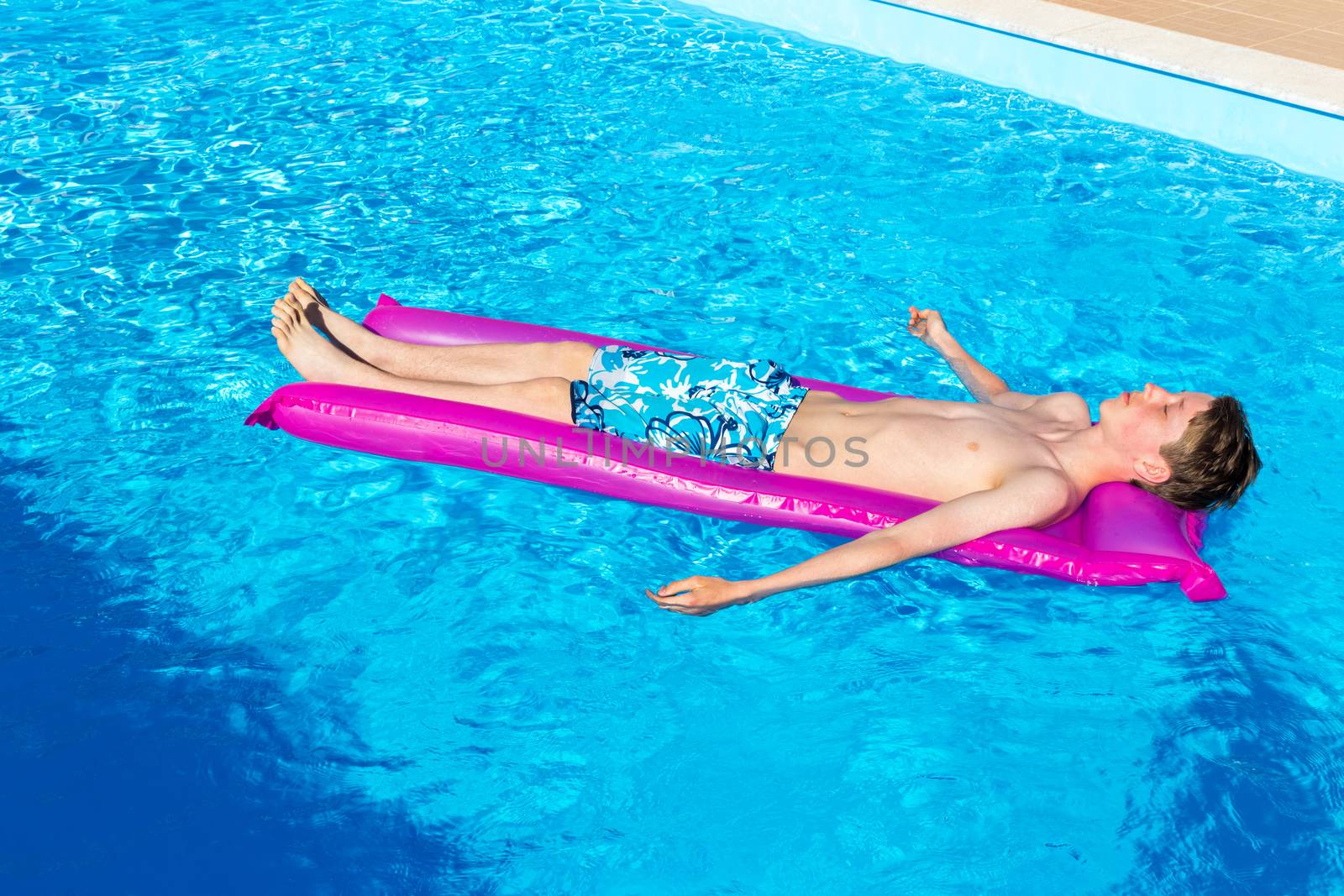 Caucasian teenage boy lying  on air mattress in swimming pool as tourist on vacation in summer