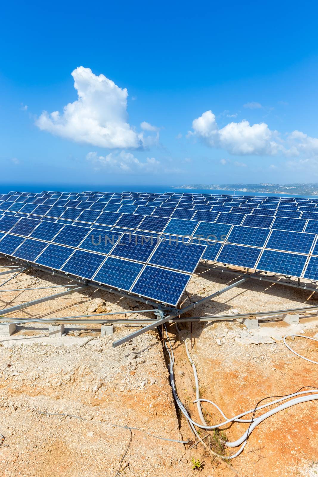 Rows of solar panels near sea with blue sky by BenSchonewille