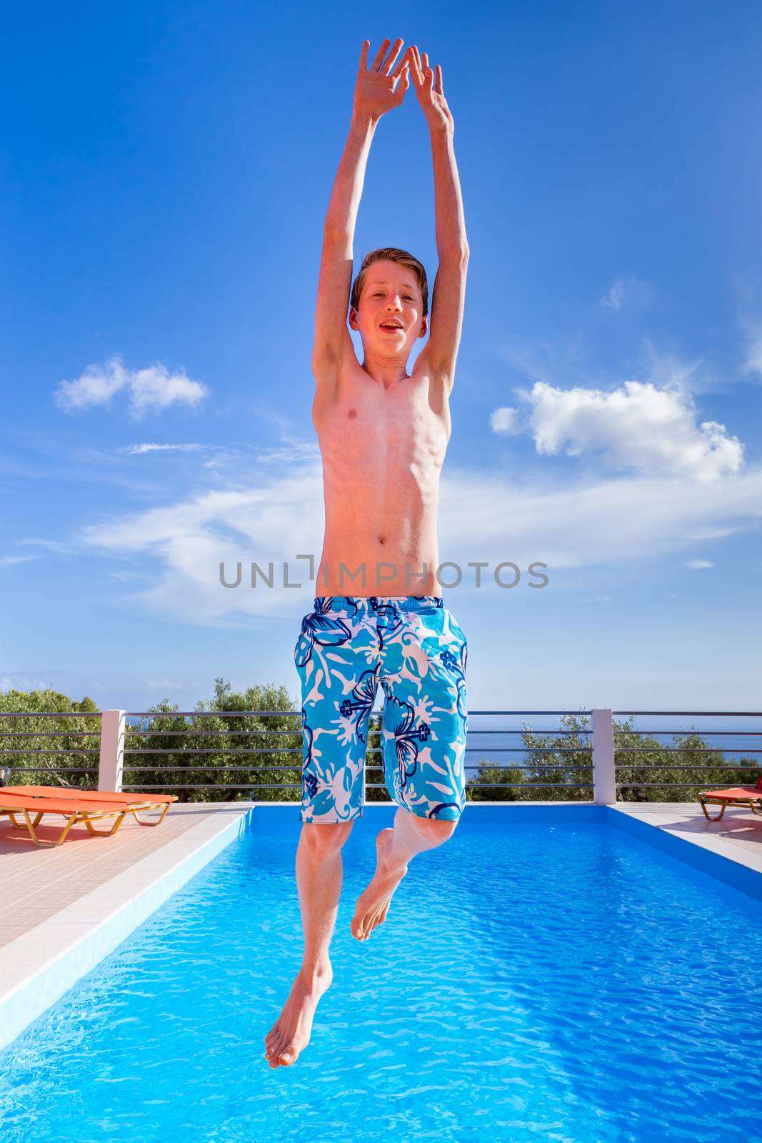 European teenage boy jumping high above blue swimming pool