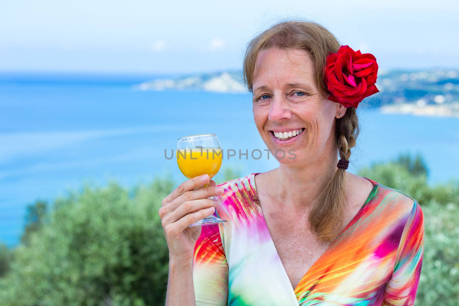 European middle aged woman with red rose holding drink near sea on vacation