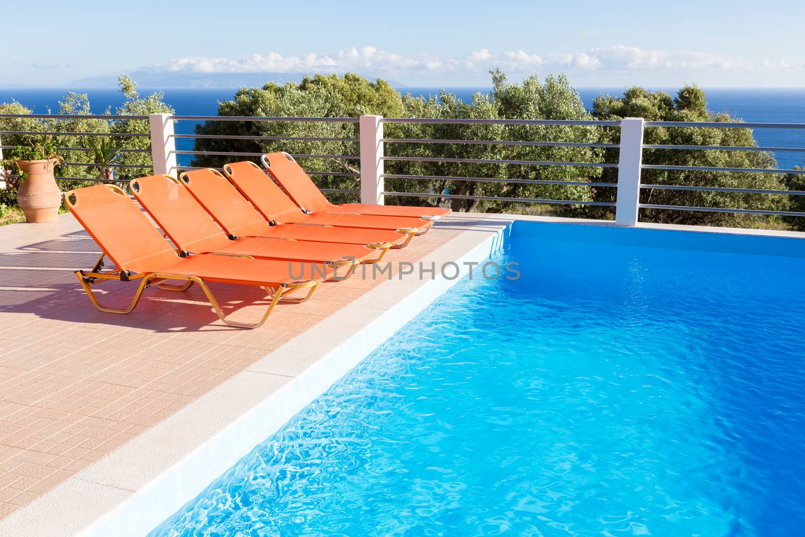 Row of orange loungers near blue swimming pool by BenSchonewille