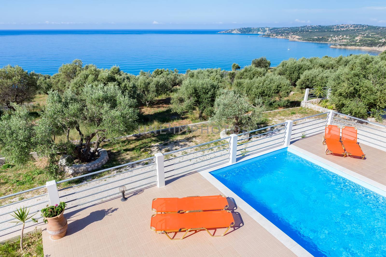 Sunloungers on terrace with blue swimming pool near sea at coast in Greece
