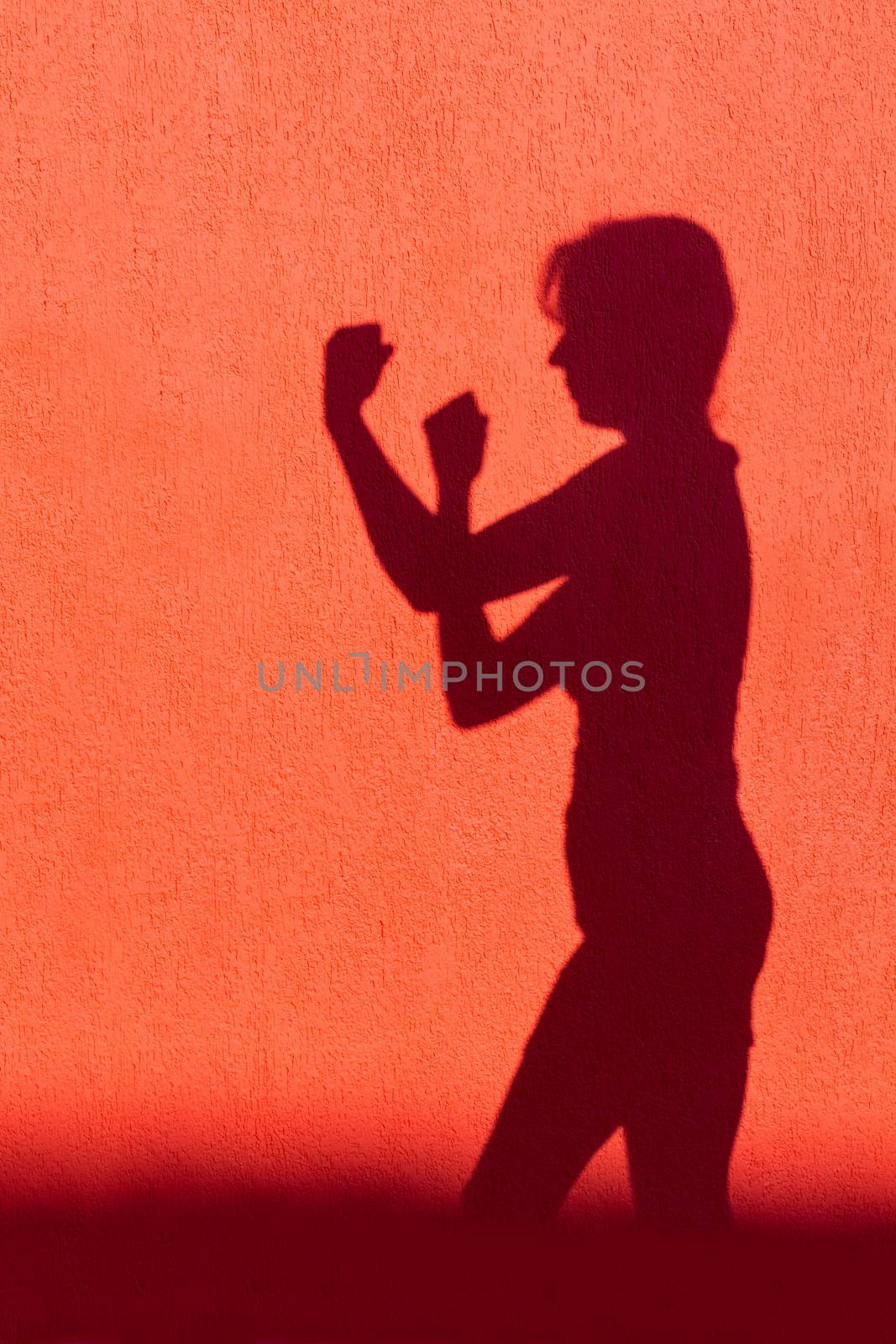 Silhouette of woman showing fists on red wall by BenSchonewille