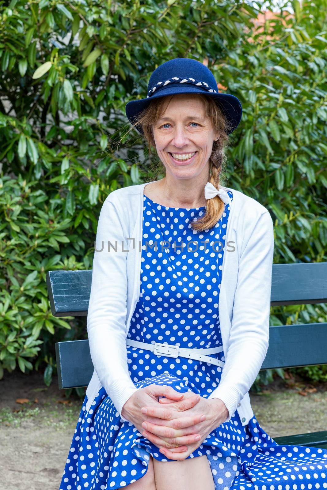 Dutch woman in old-fashioned clothes sitting on bench in park by BenSchonewille