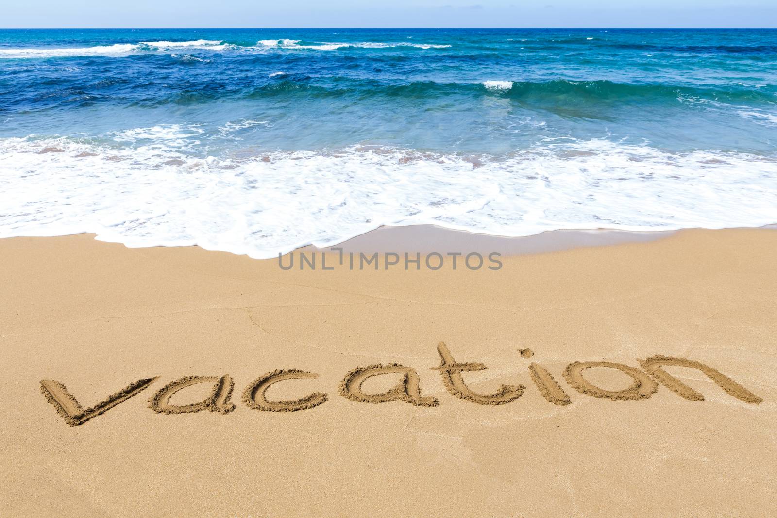 Word vacation written in sandy beach at coast with blue sea and waves