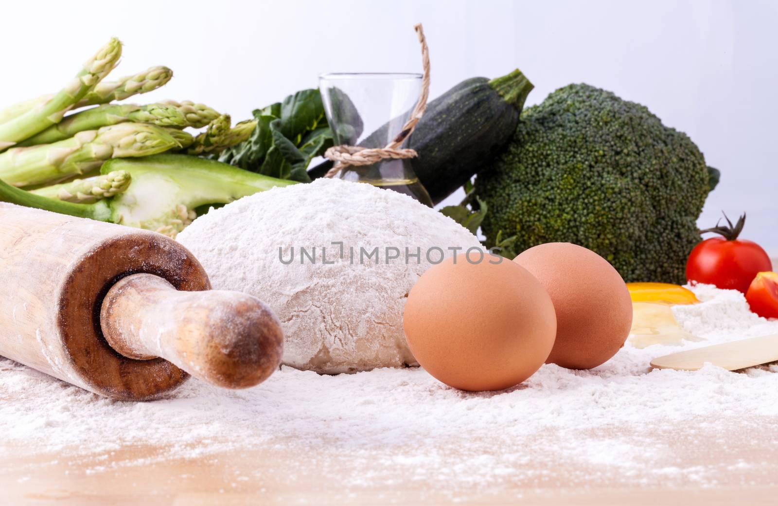 Pizza dough and ingredients flour and a rolling pin on wooden table.