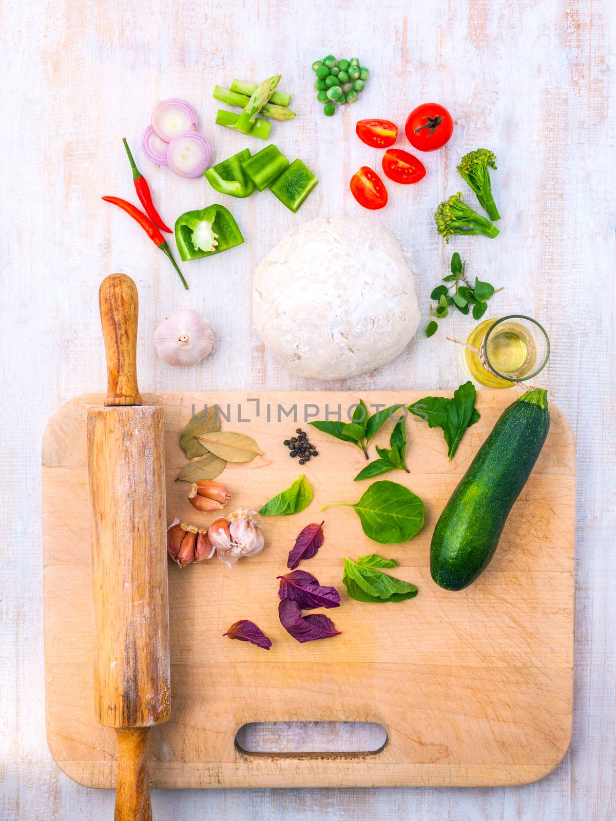 Pizza dough and ingredients flour and a rolling pin on wooden ta by kerdkanno