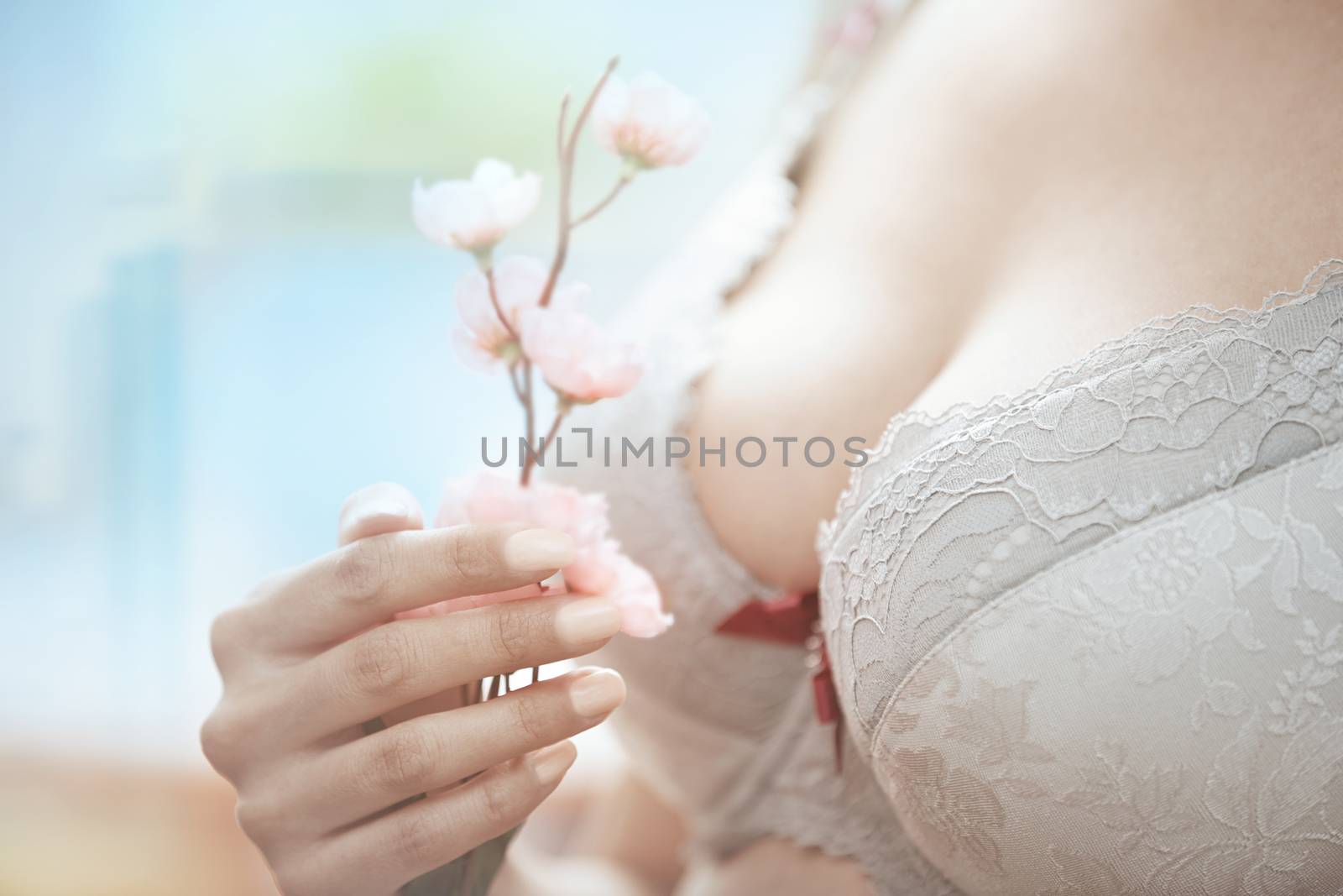 Woman in brassiere holding Sakura flower. Close-up horizontal photo