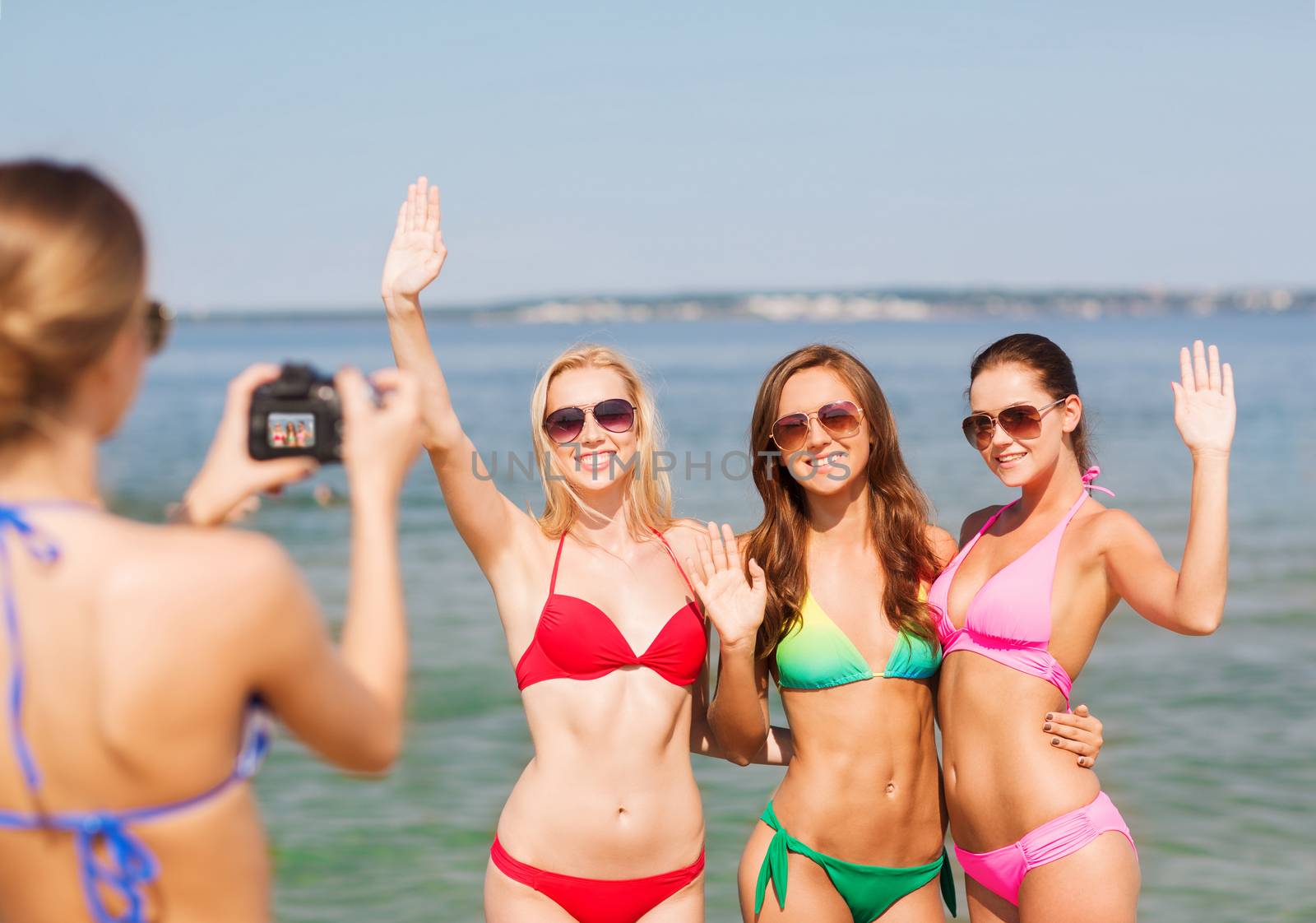 summer vacation, gesture, travel and people concept - group of smiling young women photographing by camera and waving hands on beach