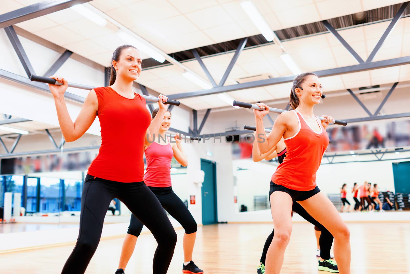 fitness, sport, training, gym and lifestyle concept - smiling trainer in front of the group of people working out with barbells in the gym