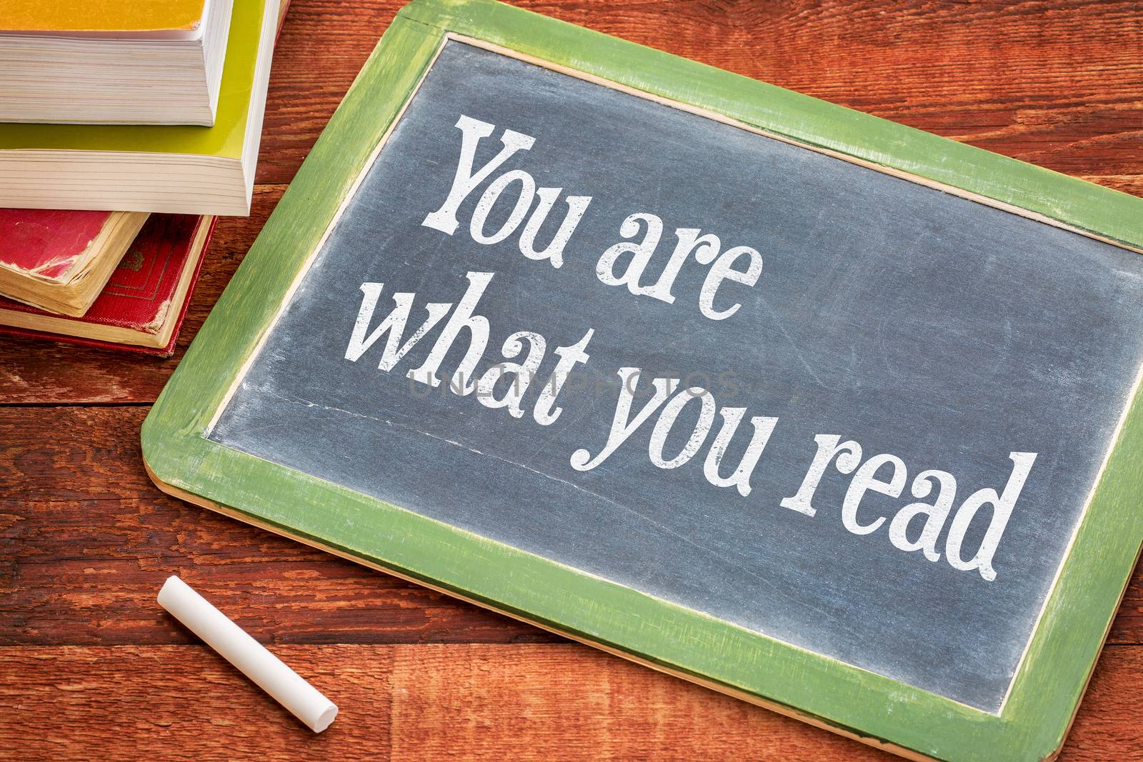 You are what you read - motivational phrase on a slate blackboard with a white chalk and a stack of books against rustic wooden table