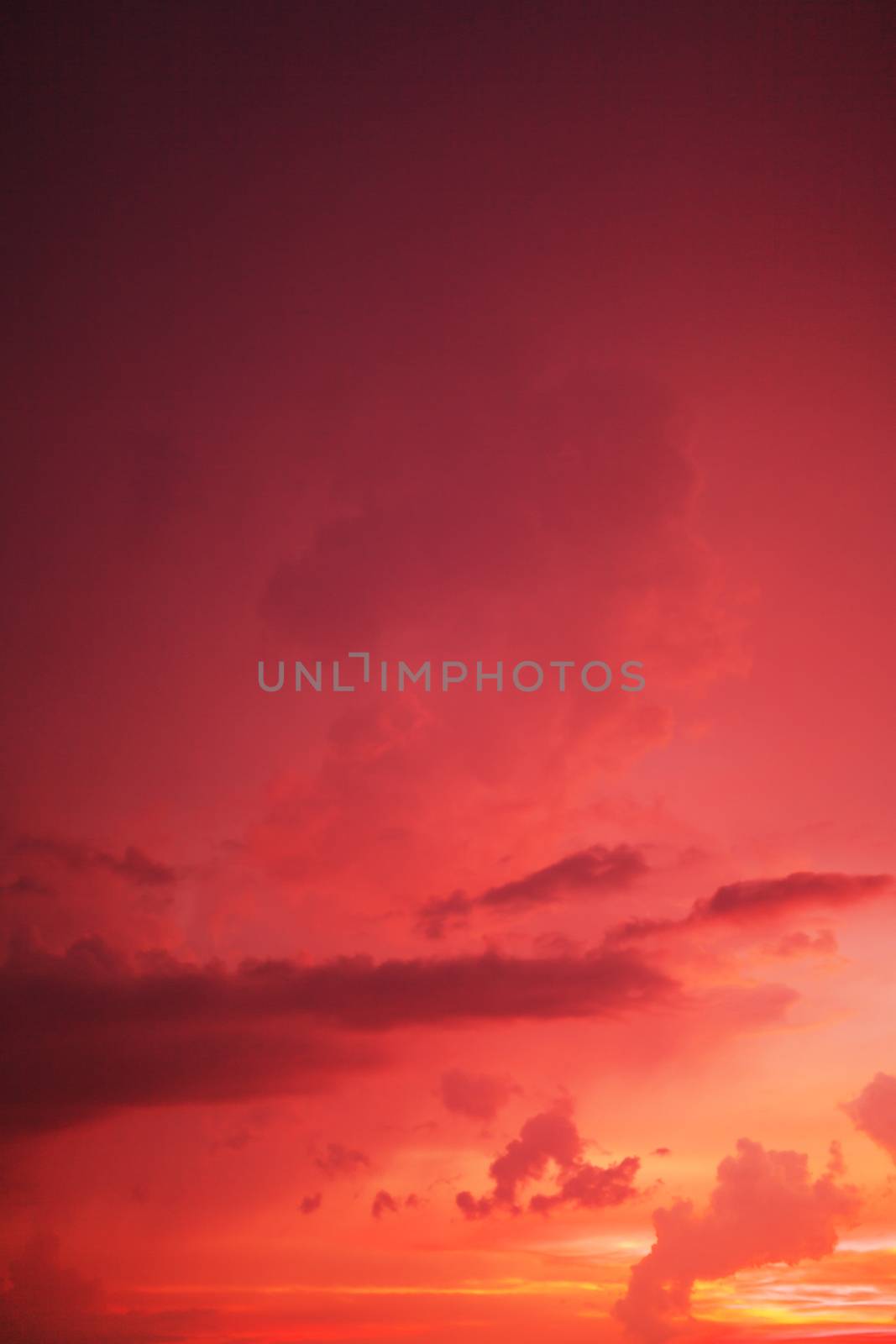 Dramatic red sunset sky with a fiery glow from the setting sun in a weather and nature full frame background, vertical orientation