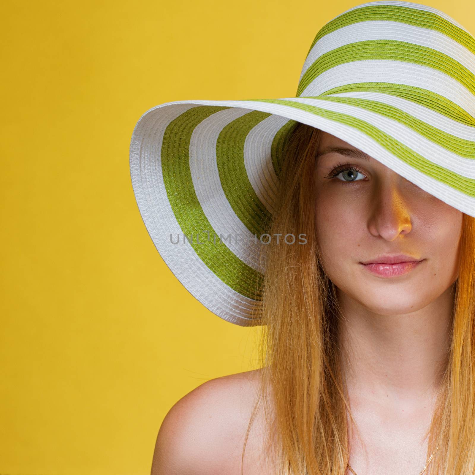 young pretty girl with a hat on her head. Yellow background. square crop