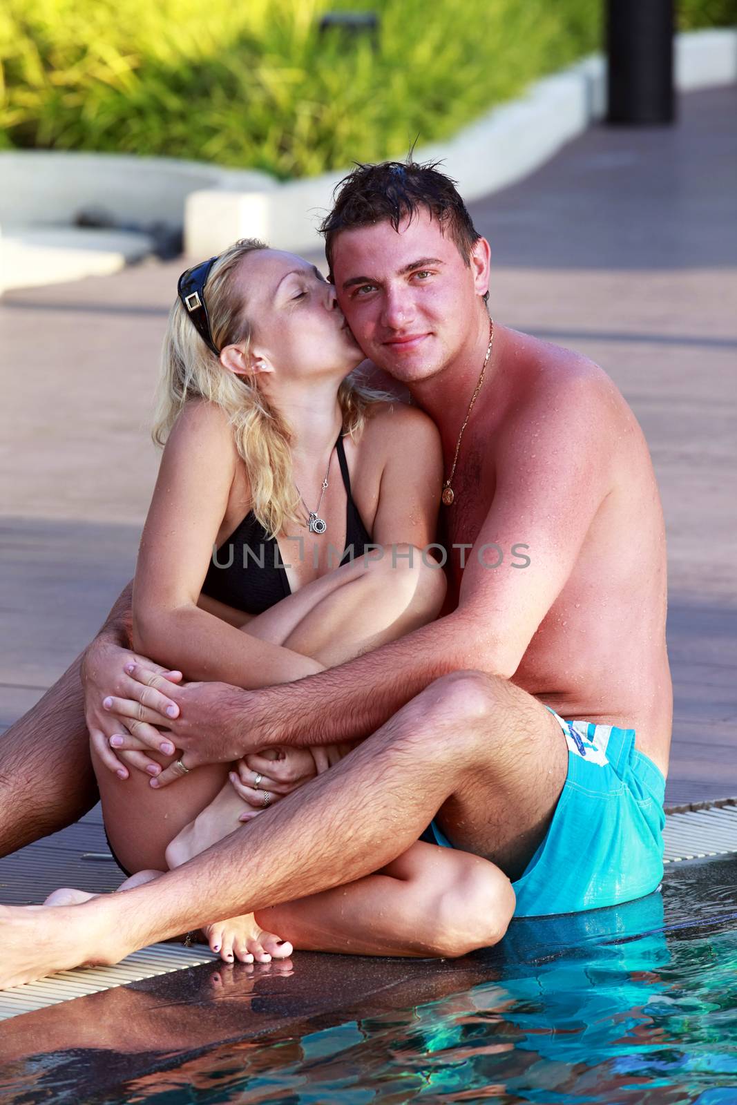 Beautiful lovers relaxing and embraces and kisses in swimming pool