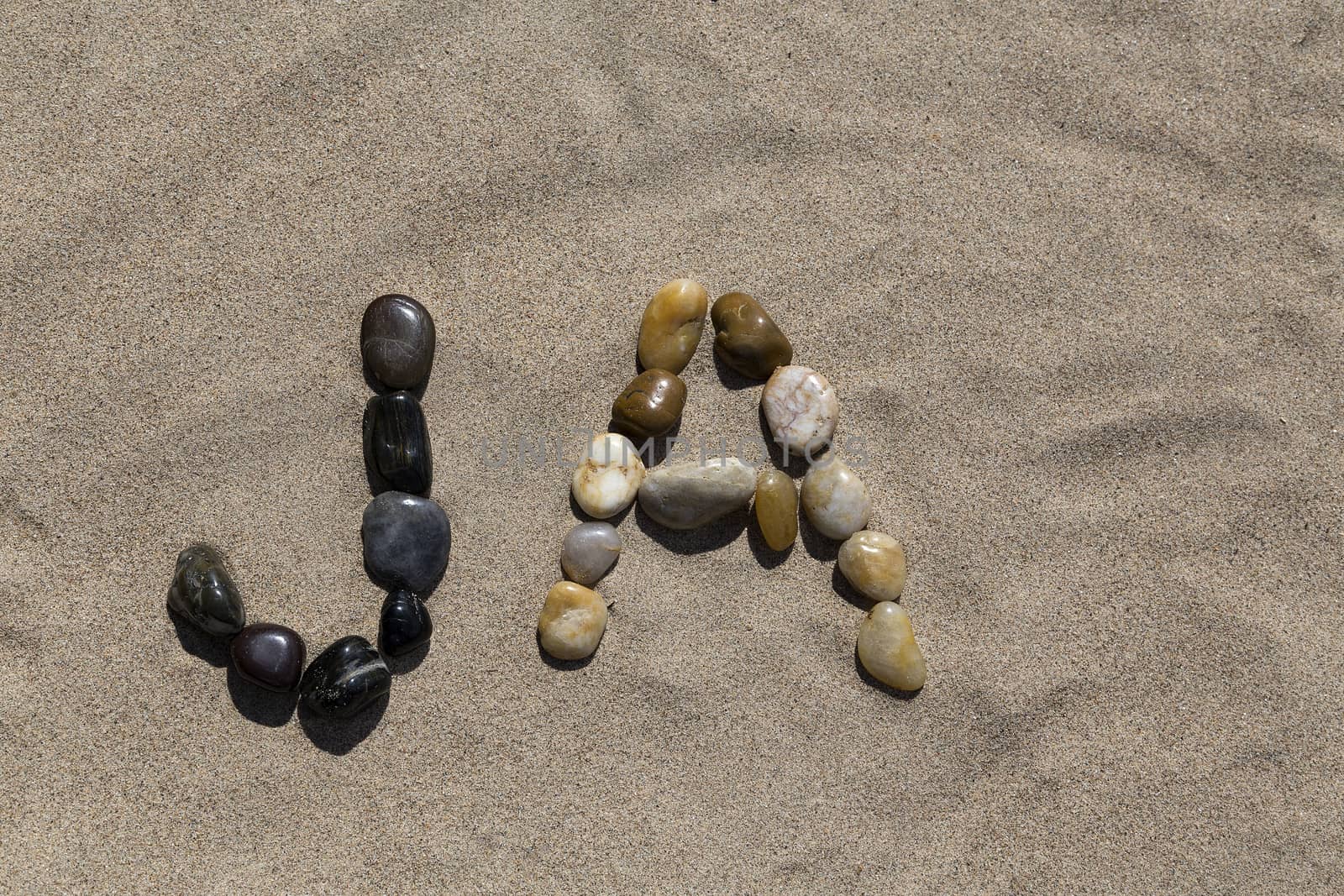 A set of pebbles in a sandy beach forming the swedish word for Yes