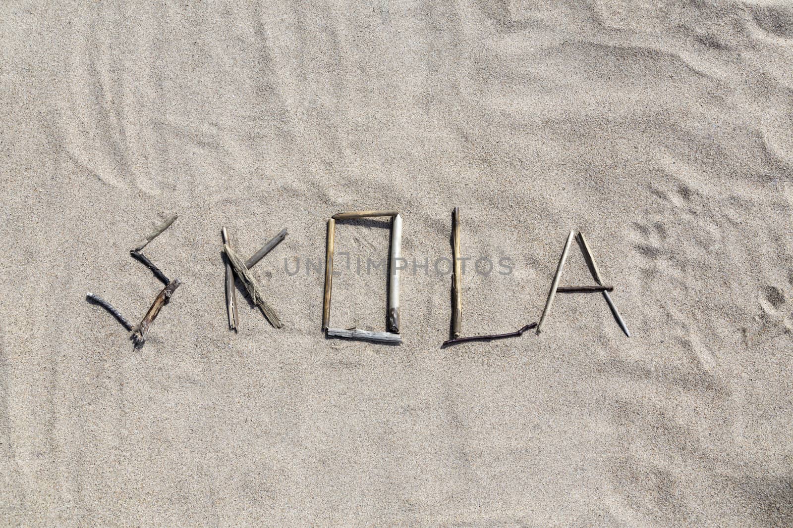 A set of sticks in a sandy beach forming the swedish word for school