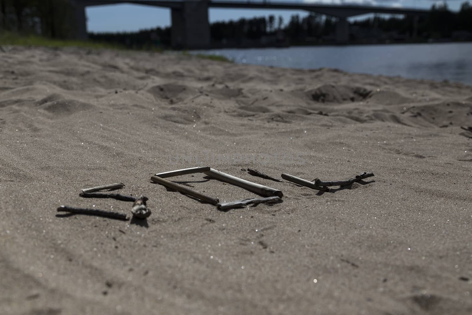 A set of sticks in a sandy beach forming the swedish word for sun and a bridge in the background