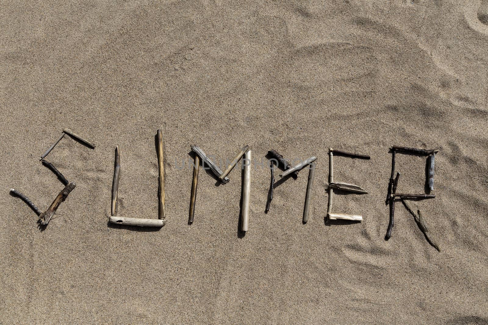 A set of sticks in a sandy beach forming the word Summer